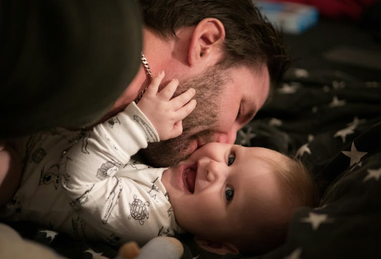 A happy, smiling baby and a dad with a beard kissing her cheek.